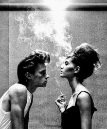 a man and a woman are smoking cigarettes and looking at each other .