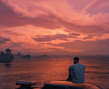 a man sits on the back of a boat looking at the sunset over the ocean