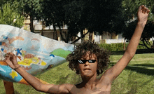 a shirtless boy wearing sunglasses is holding a painting