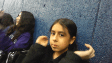 a girl sitting in front of a blue wall with a purple shirt that says ' a ' on it