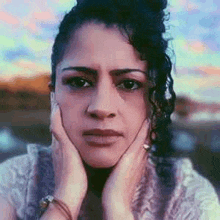 a woman with curly hair is holding her face with her hands and making a sad face .