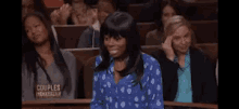 a woman in a blue polka dot shirt is sitting in a courtroom with a couples court sign behind her