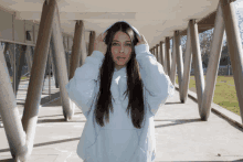 a woman wearing a light blue hoodie stands in a hallway