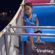 a young boy is sitting on a slide at a carnival and the words viralhog are on the bottom of the slide .