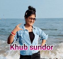 a woman in a denim jacket stands in front of the ocean with the name khub sundor written on the bottom