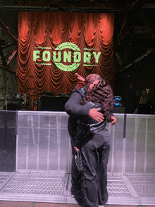 two people hugging in front of a stage that has the word foundry on it