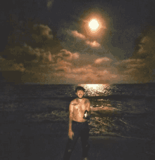 a shirtless man stands on the beach holding a beer