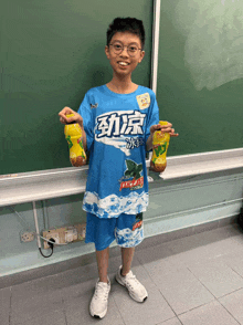 a boy in a blue shirt with chinese writing on it is holding two bottles