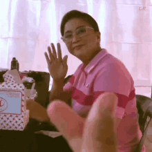 a woman wearing glasses and a pink shirt is waving her hand