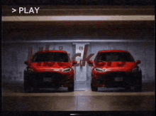 two red cars are parked next to each other in a garage with the word play visible in the corner