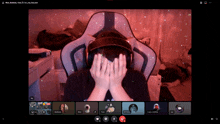 a person covering their face with their hands while sitting in a chair on a video call