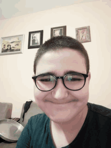 a young boy wearing glasses makes a funny face in front of a wall with pictures on it