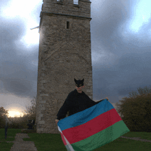 a man wearing a batman mask holds a flag in front of a stone tower