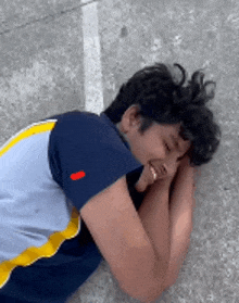 a young man in a blue and yellow shirt is laying on the ground .