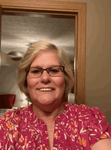 a woman wearing glasses and a pink top smiles for the camera