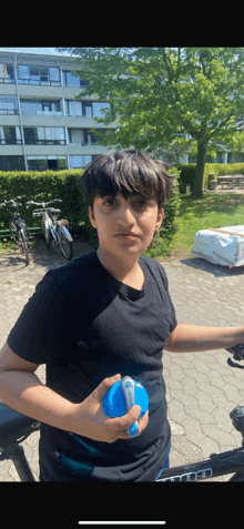 a boy in a black shirt holds a blue bottle in front of a bicycle