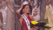 a woman in a red dress is holding a bouquet of yellow flowers and wearing a miss universe sash .