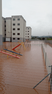 a flooded playground with a fence and a building in the background