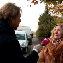 a woman in a fur coat is being interviewed by a man holding a microphone that says tdp on it