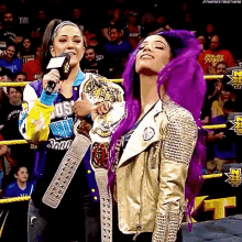 a woman with purple hair is holding a championship belt while standing next to another woman in a wrestling ring .