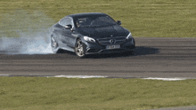 a black mercedes is driving on a track with smoke coming out of the wheels