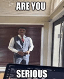 a man in a suit and tie is standing in front of a laptop computer and a mirror .