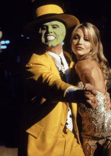 a man in a yellow suit and green mask is dancing with a woman