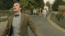 a man in a suit and bow tie is running down a street with a group of people behind him .