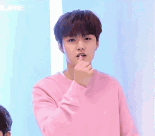 a young man in a pink sweater is making a heart with his finger