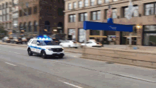 a police car is driving down a street in front of a building with a blue sign that says post office