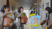 three girls are carrying bags and boxes in a hallway with a sign on the wall that says 3- 3