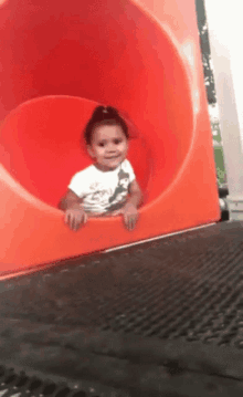 a little girl in a white shirt is going down a red slide