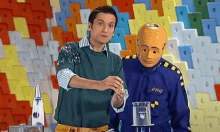 a man in a green shirt is standing next to a mannequin wearing a crash test helmet .