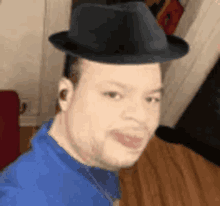 a man wearing a fedora hat and a blue shirt is making a funny face .