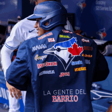 the back of a blue jays player 's jacket says la gente del barrio on the bottom