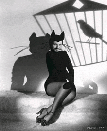 a black and white photo of a woman dressed as a cat with a bird behind her .