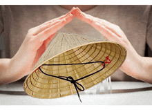 a person is holding a straw hat with their hands in the shape of a house