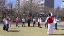 a man in a red jacket with the word russia on it is standing in front of a group of children on a field .