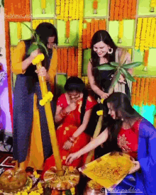 a group of women are gathered in a room with flowers in the background and one of them is holding a tray of food