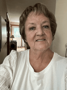 a woman in a white shirt is smiling in front of a door