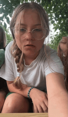 a girl wearing glasses and a bracelet is sitting on a bench