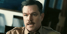 a man with a mustache is wearing a tan uniform