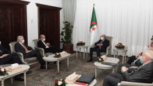 a group of men wearing face masks are sitting around a table with a flag in the background