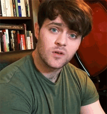 a man wearing a green shirt is standing in front of a bookshelf with a book titled the hobbit in it