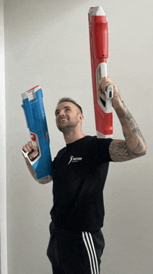 a man wearing a black shirt that says motion is holding two water guns over his head