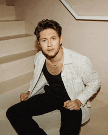 a man is sitting on a set of stairs wearing a white shirt and black pants