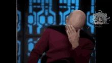 a bald man is covering his face with his hand while sitting in a chair .