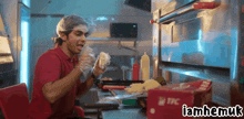 a man in a red shirt is eating a sandwich in a kitchen with a box of tfc behind him