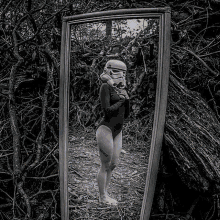 a black and white photo of a woman in a storm trooper costume taking a selfie in a mirror .