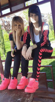 two girls are sitting on a bench wearing nike shoes